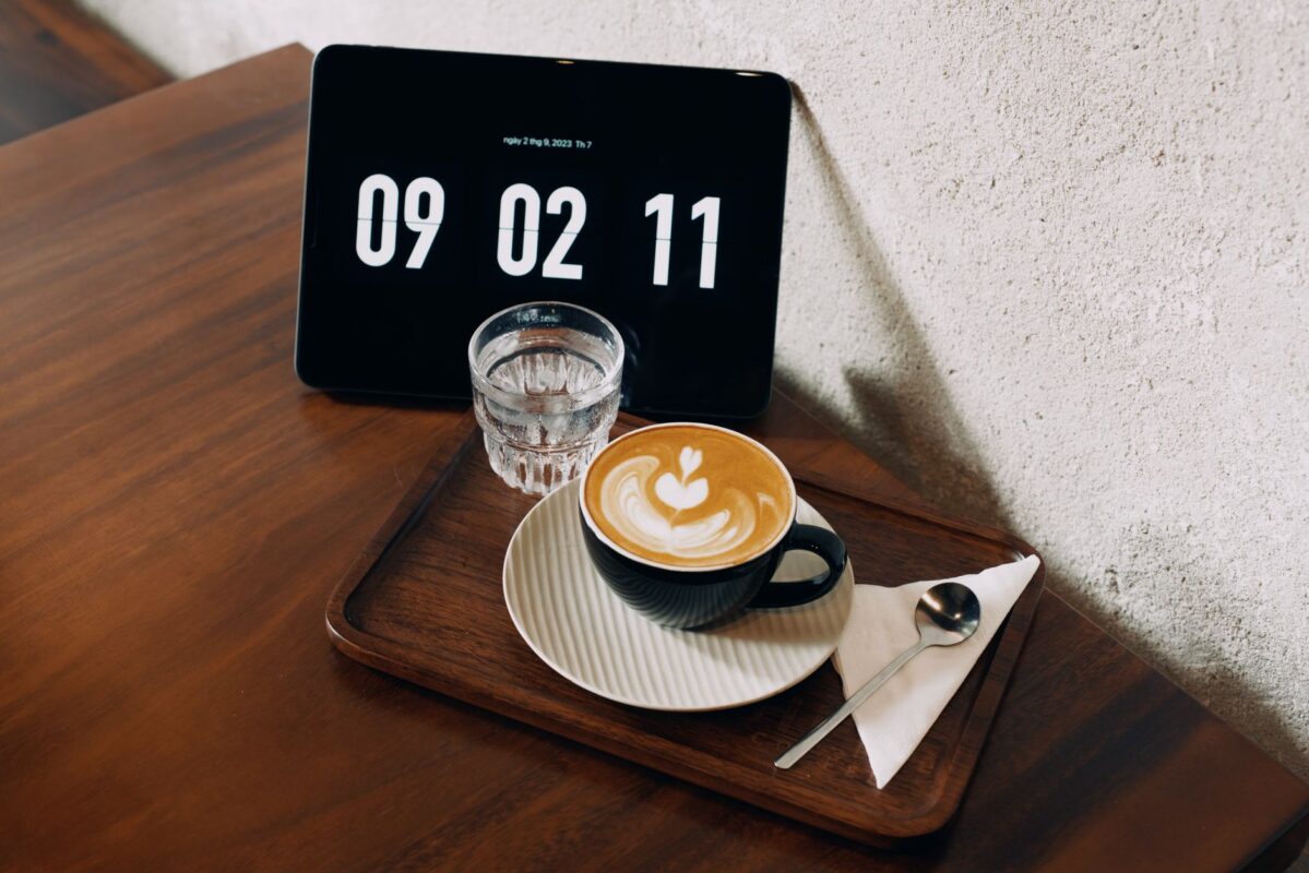 Cup of coffee on a wooden tray beside a clock showing the morning time