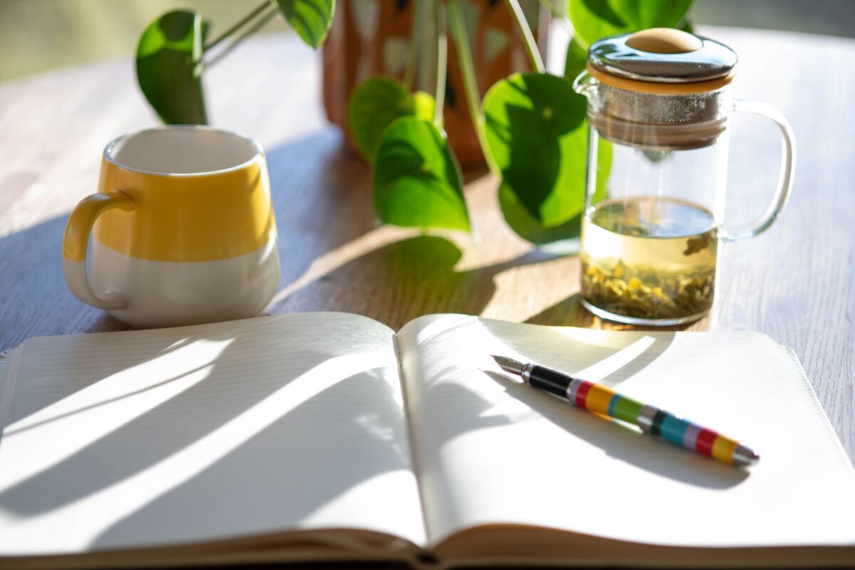 Sunlit desk with an open notebook, pen and a cup of tea