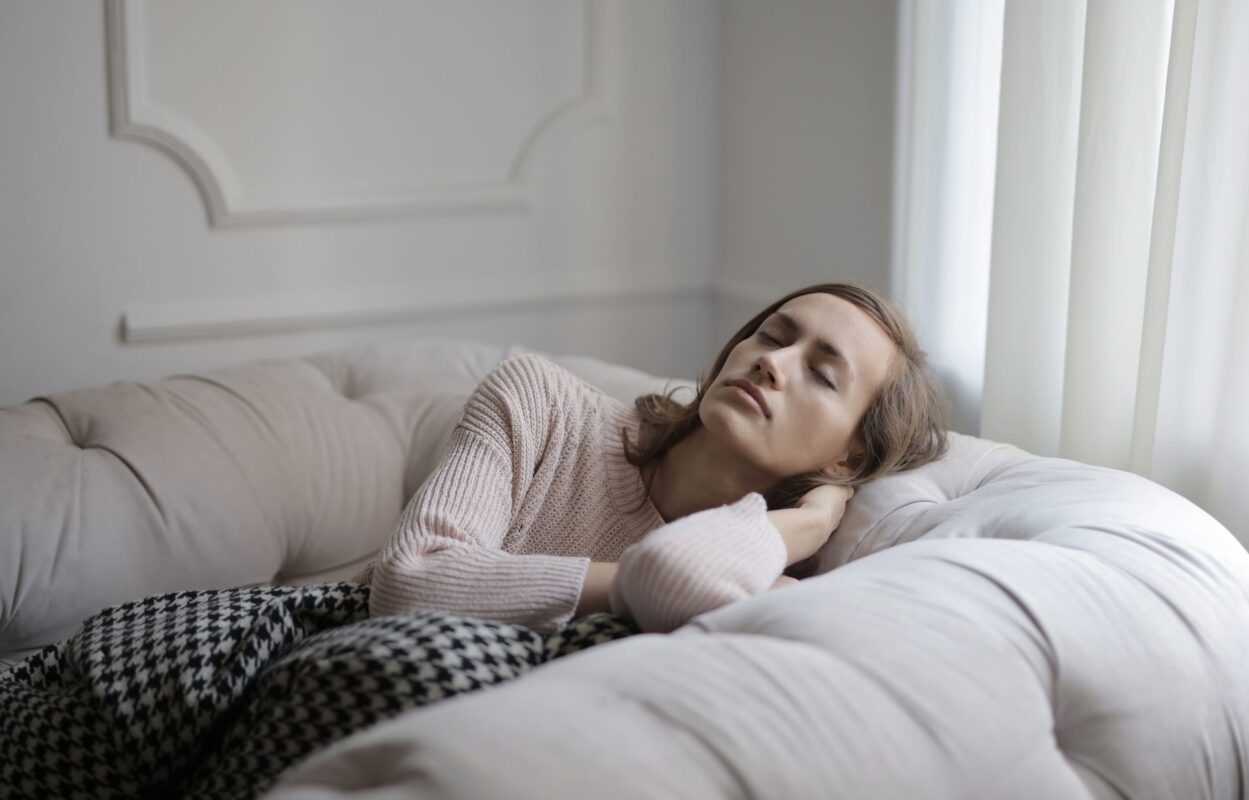 Woman in a cosy jumper relaxing on a sofa with eyes closed