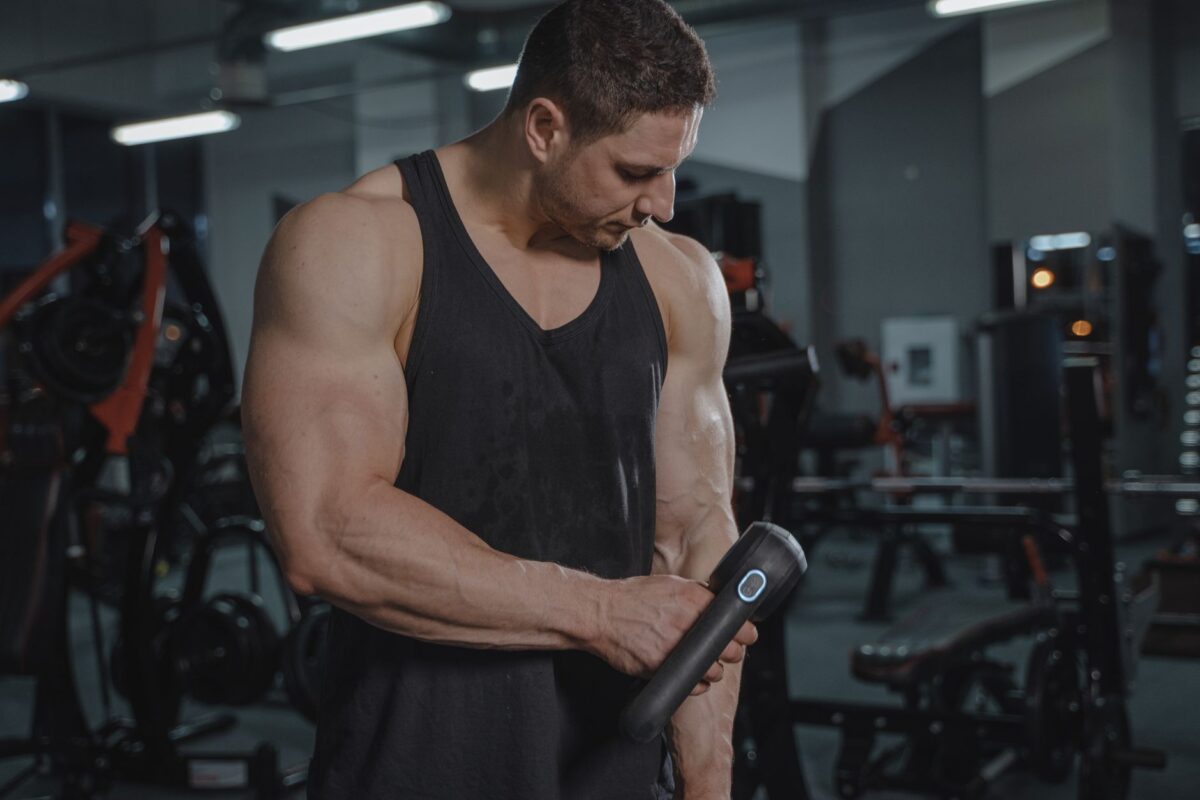 Man using a massage gun on his forearm in a gym