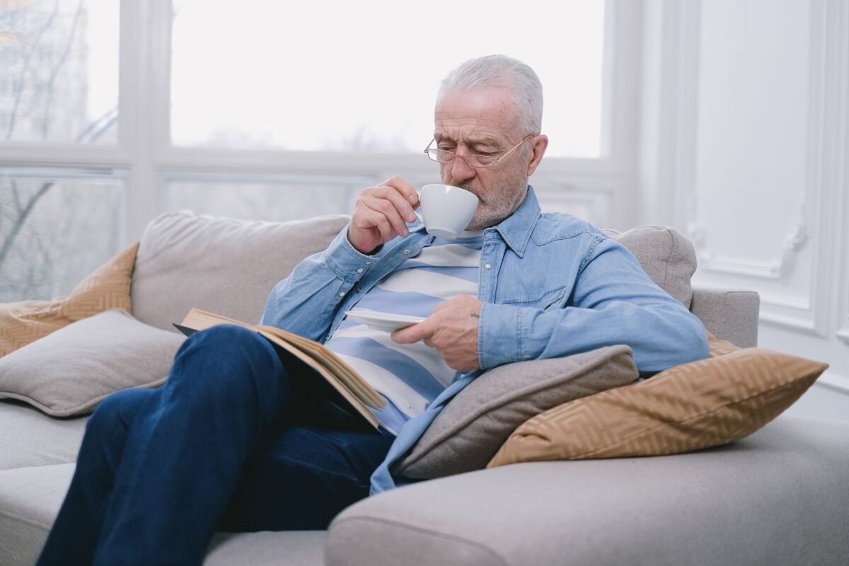 Older man relaxing on a sofa with a cup of tea and a book