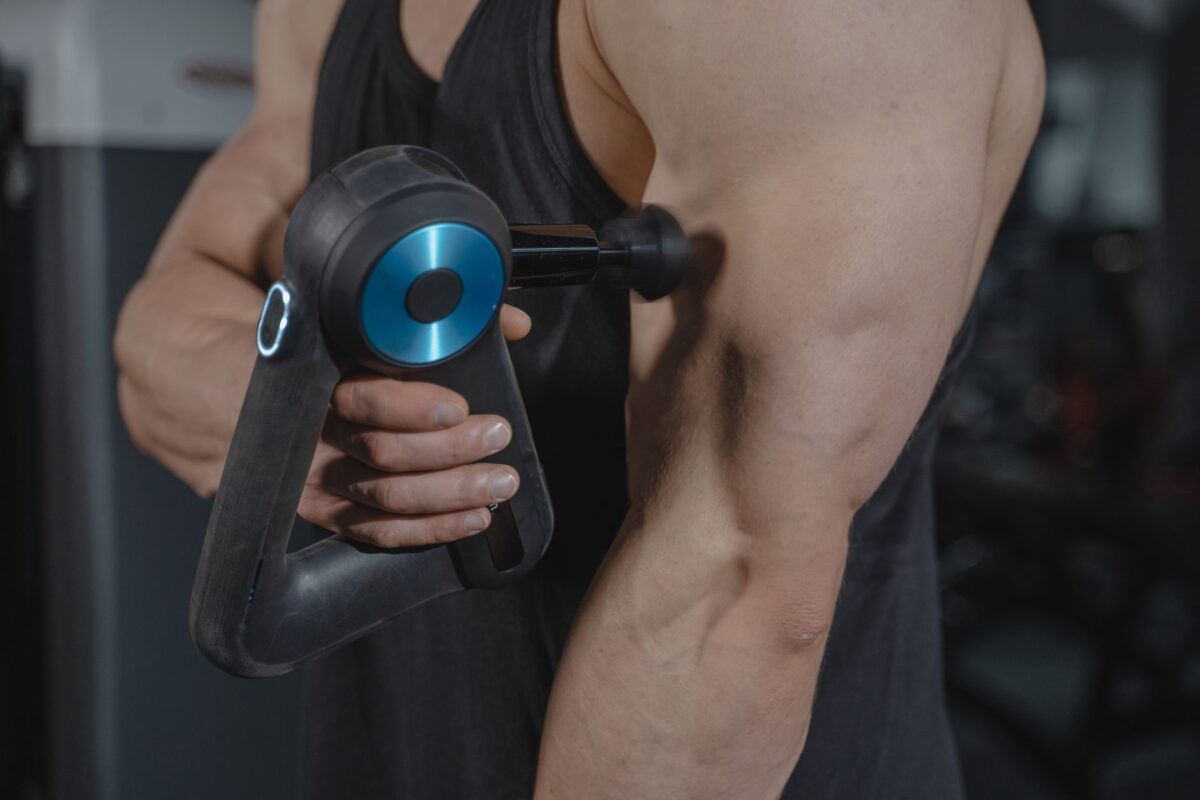Man using a massage gun on the muscle of his upper arm