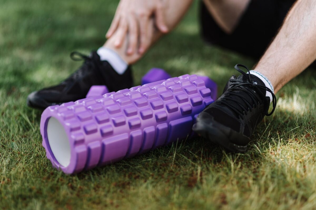 Purple foam roller on grass beside a person in trainers