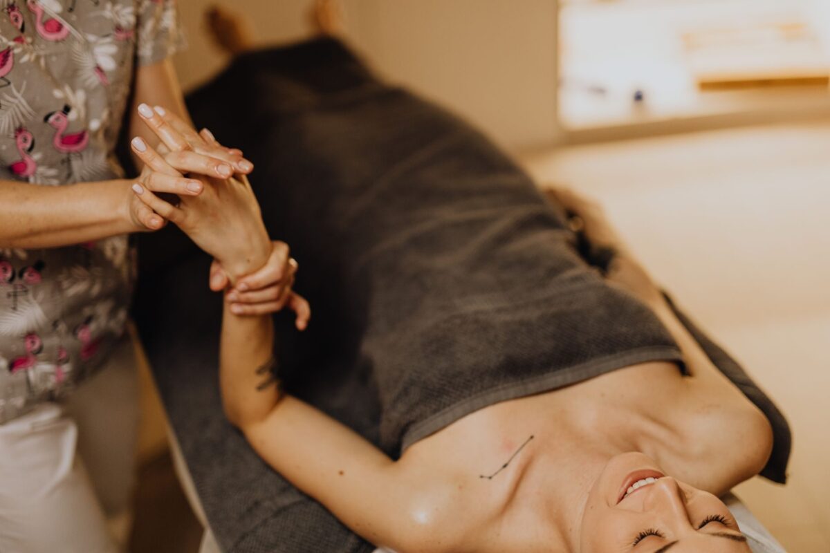 Therapist gently pressing a relaxed, towel-draped client's hand and forearm during a massage