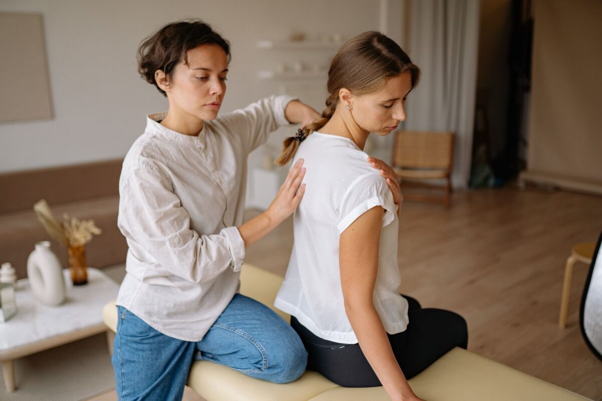Therapist standing behind a seated, fully clothed client with her hands on the client's back and shoulder