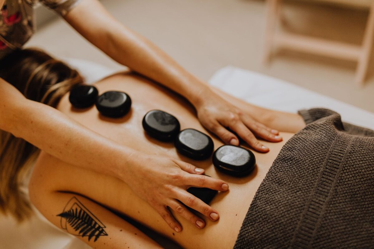 Smooth black massage stones lined up along a client's back while the therapist's hands glide over them